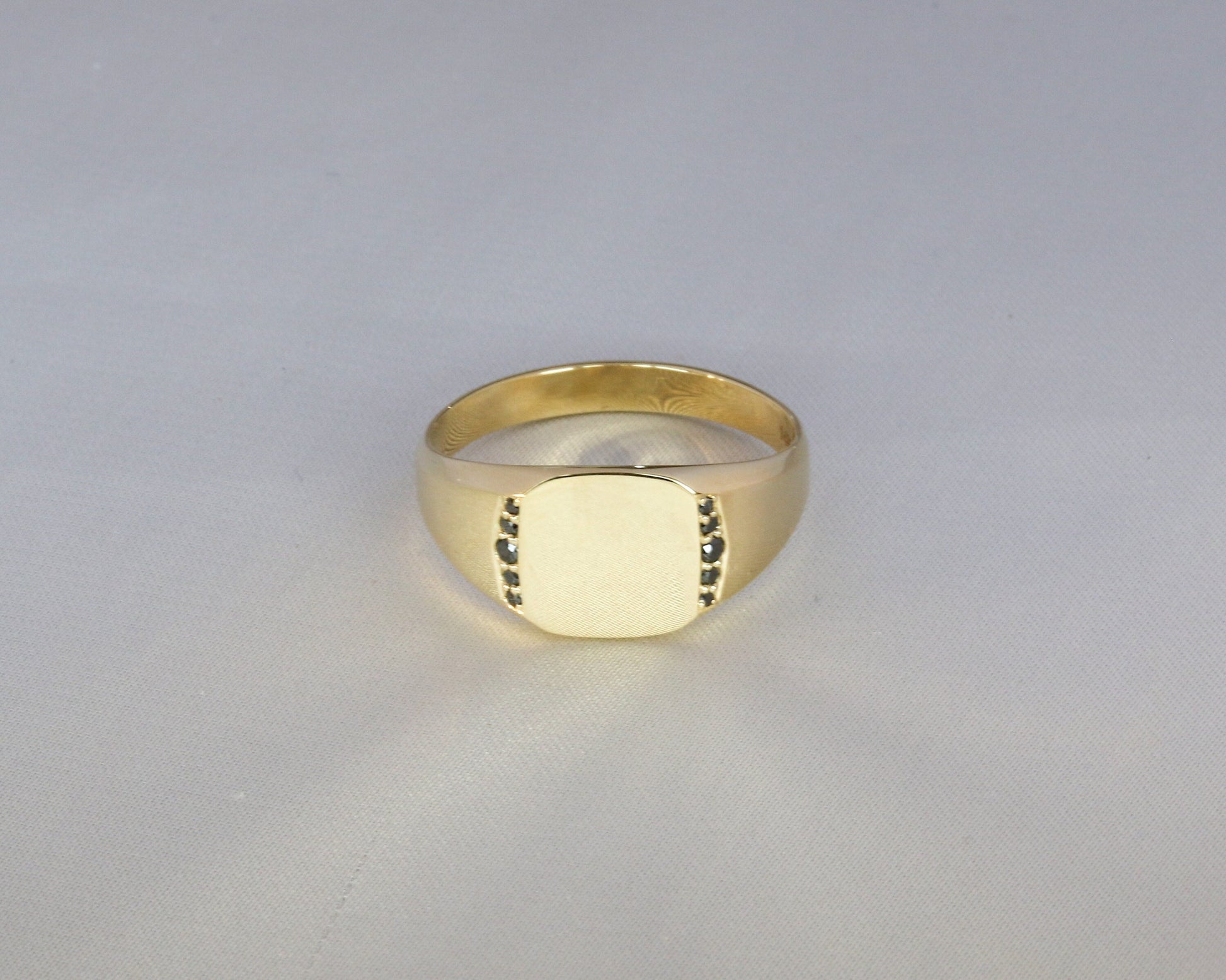 Men’s 14K gold signet ring with black diamonds set along the sides, shown on a light gray background.