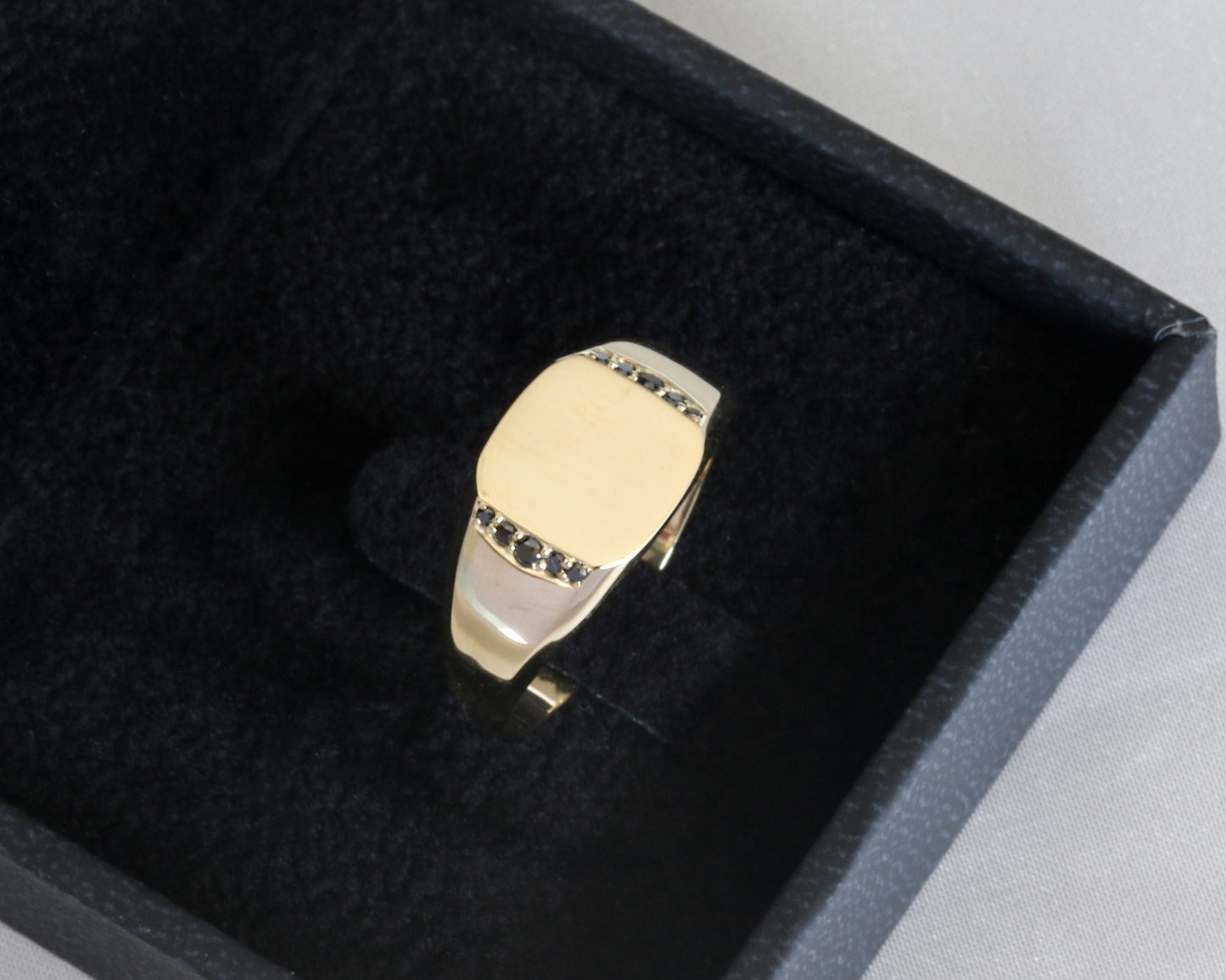 Men’s 14K gold signet ring with black diamonds set along the sides, displayed in a black jewelry box.