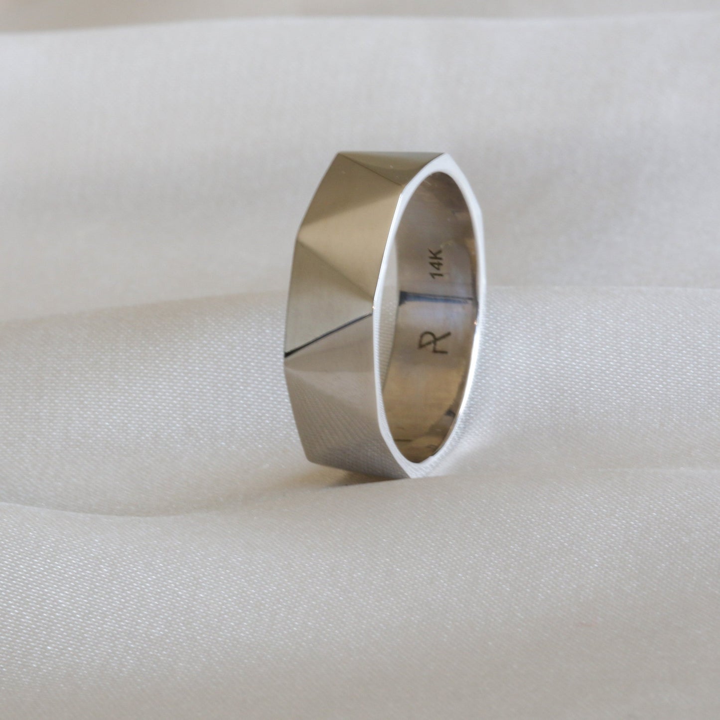 triangle faceted white gold ring on the side on white cloth
