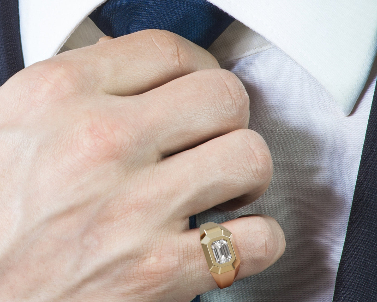 Men’s 14K gold signet ring with a light-colored emerald-cut gemstone, worn on a hand holding a suit jacket.