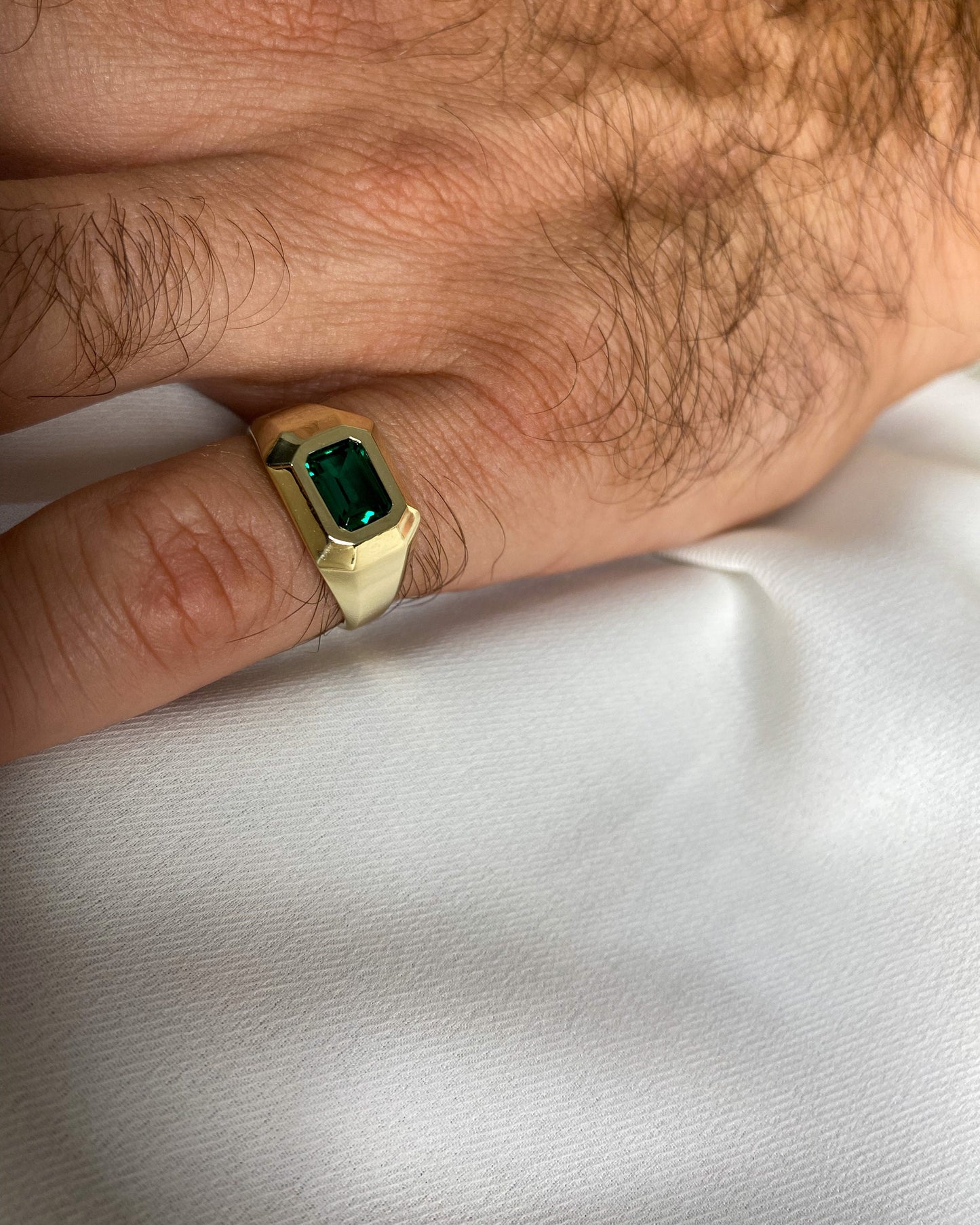 Men’s 14K yellow gold signet ring with emerald-cut Chatham emerald worn on a male hand against a white background