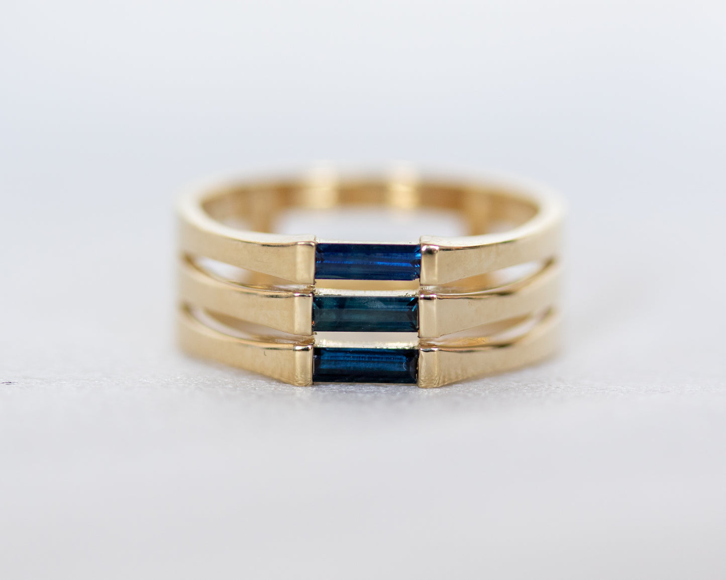 A minimalist gold ring with three blue baguette cut sapphires set close together, creating a light and unique appearance