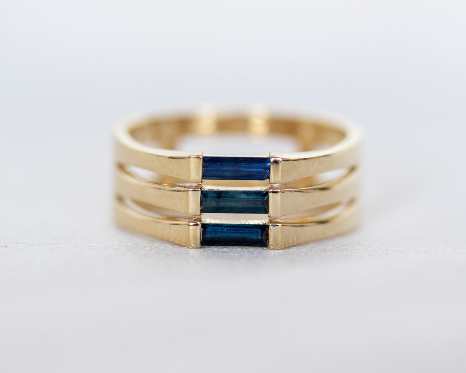A minimalist gold ring with three blue baguette cut sapphires set close together, creating a light and unique appearance