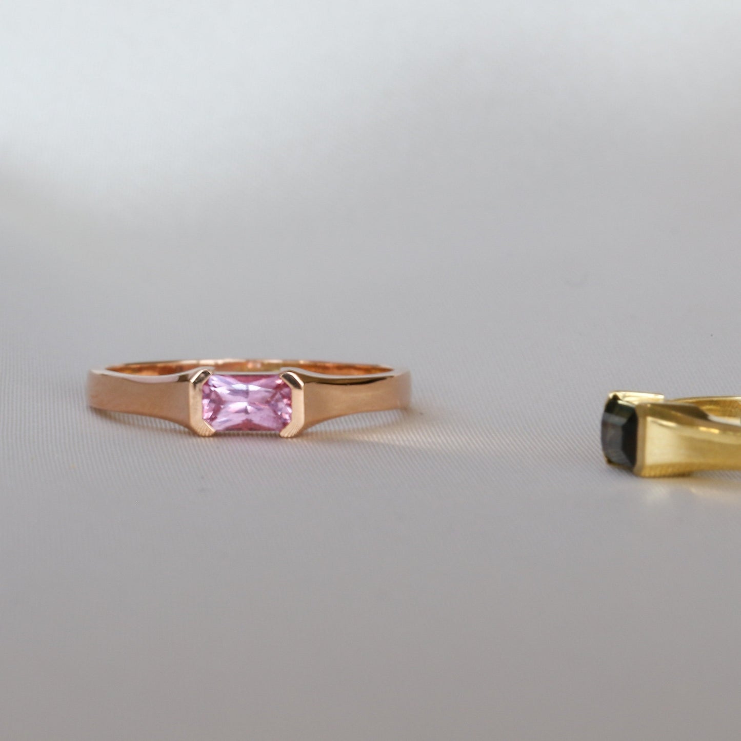A rose gold ring with a emerald cut natural pink sapphire stone, set in a half bezel setting.