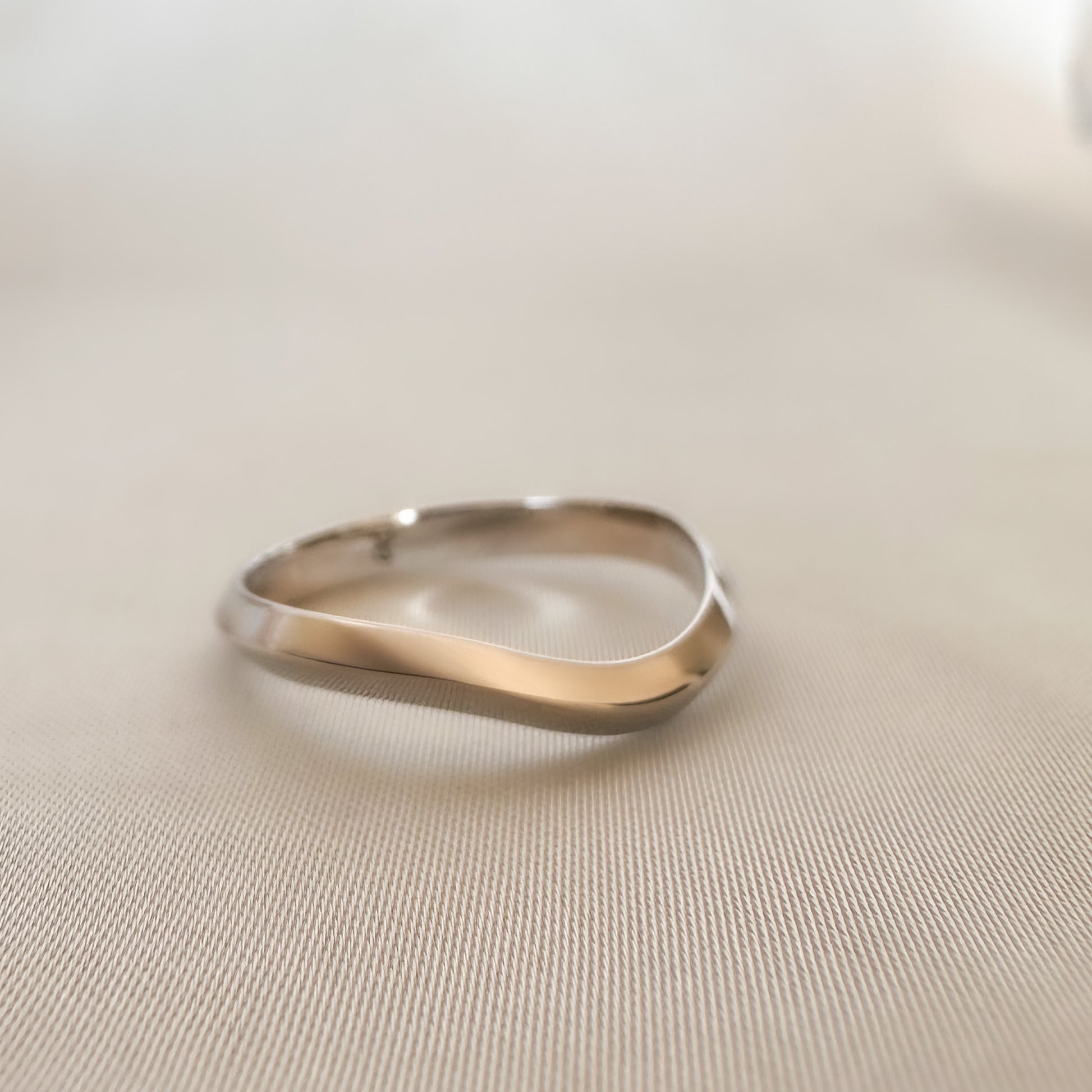 A 14K gold ring with a modern geometric wavy design, sitting on a textured surface.