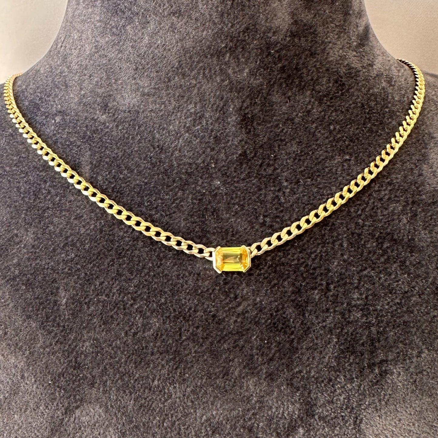 A 14K gold yellow sapphire solitaire necklace with an emerald cut natural diamond pendant on a gray textured jewelry torso