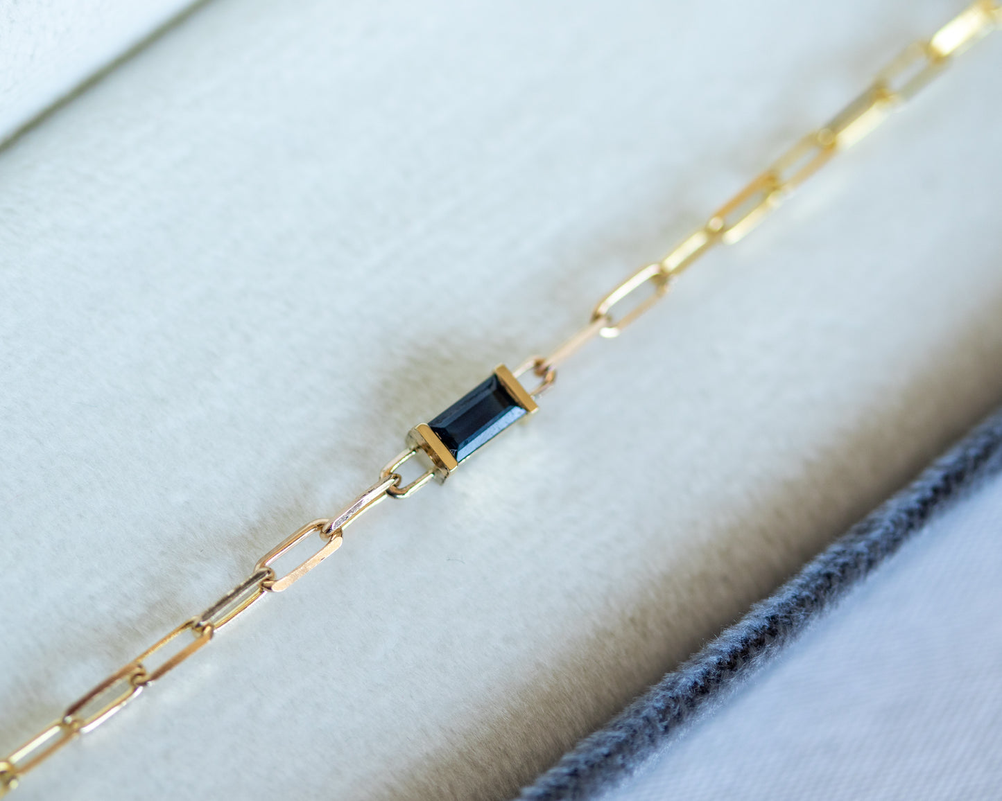 Gold bracelet with a blue baguette cut sapphire on white background
