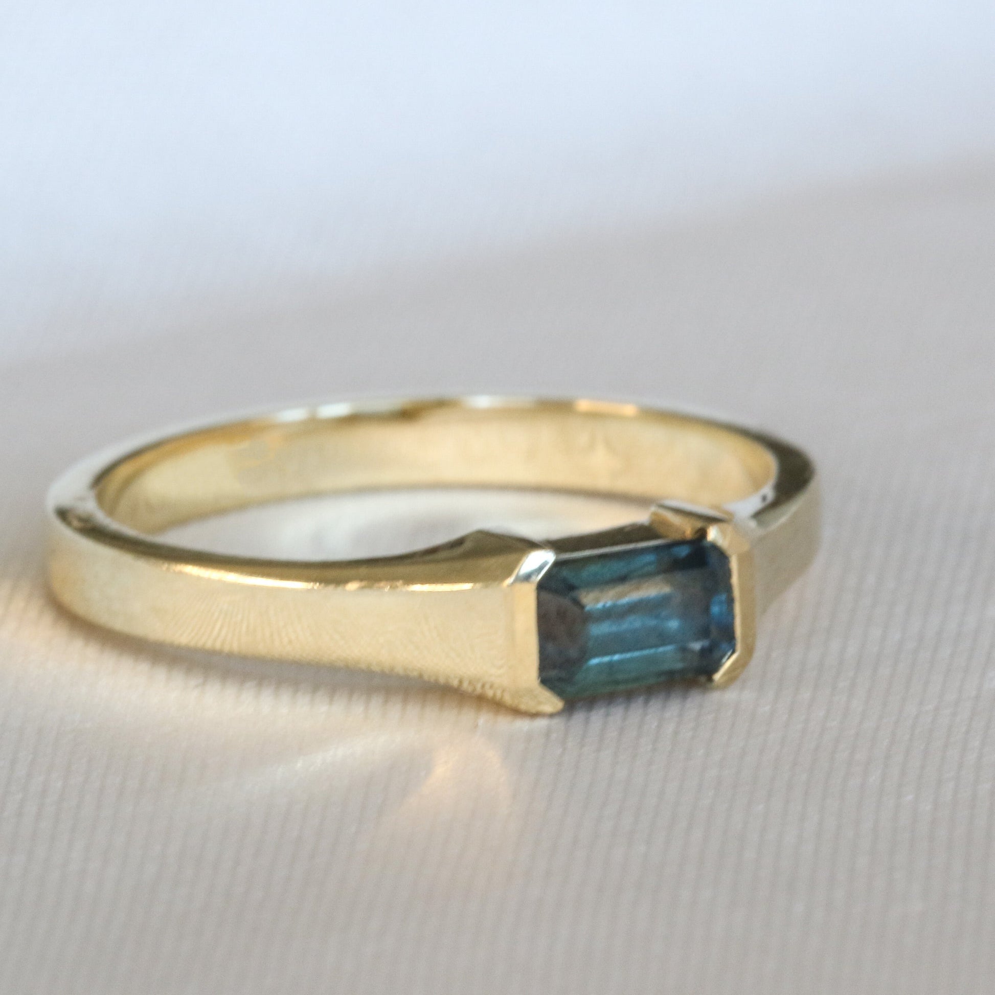 A gold ring with a emerald cut natural sapphire stone, set in a half bezel setting.