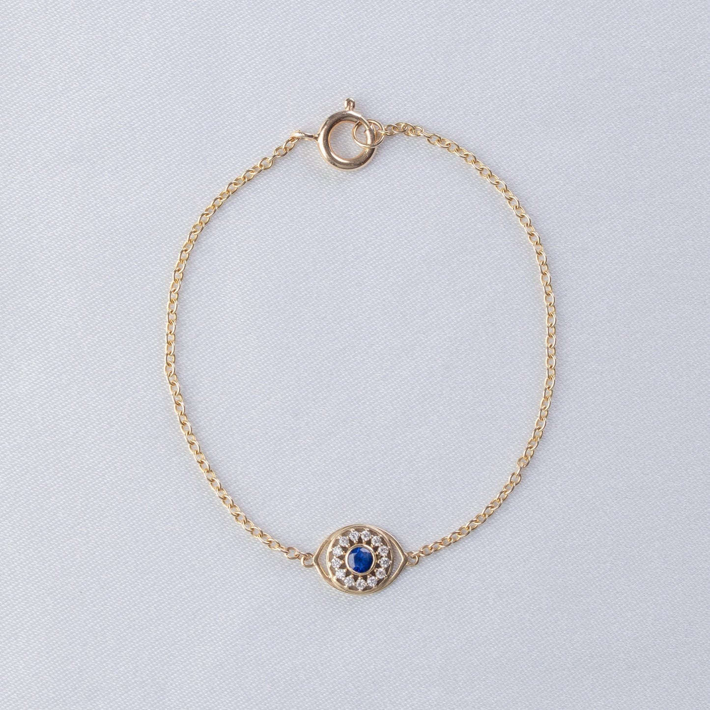Gold bracelet with a blue gemstone on a light gray background