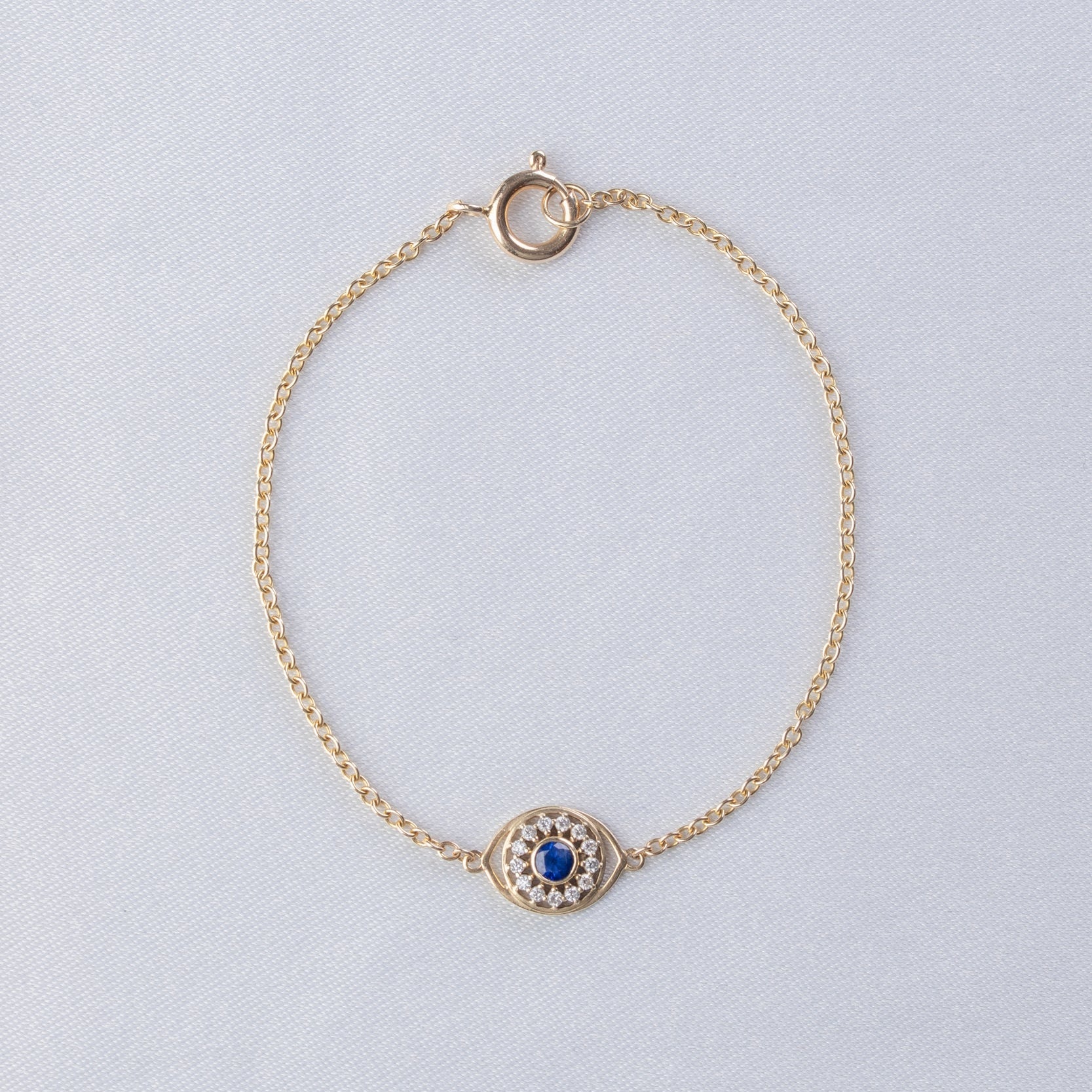 Gold bracelet with a blue gemstone on a light gray background