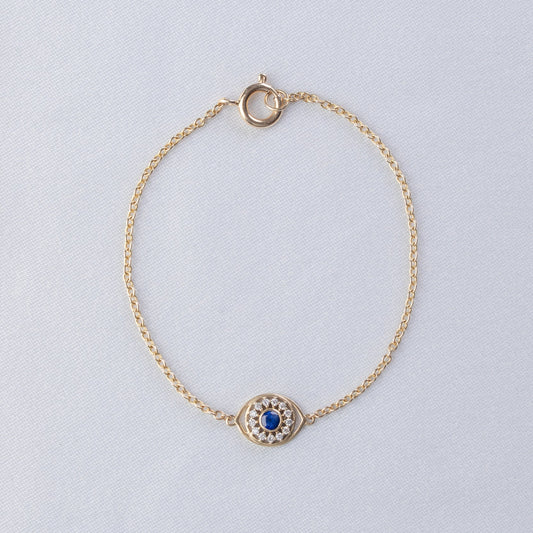Gold bracelet with a blue gemstone on a light gray background