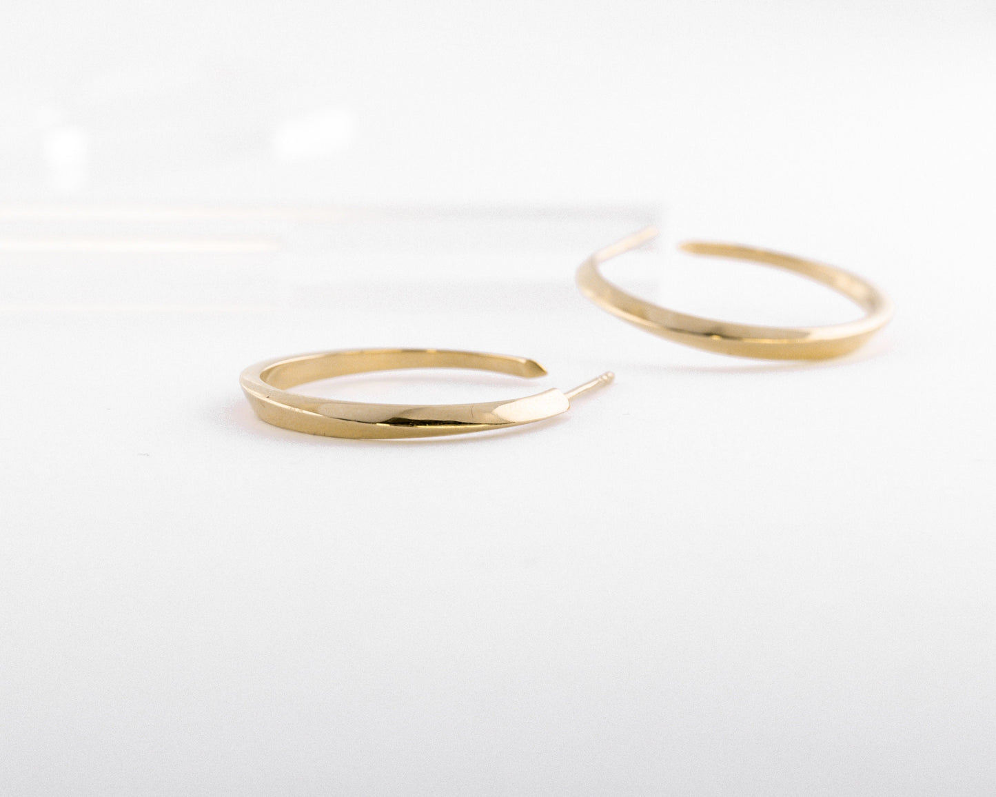 Minimalist 14K gold hoop earrings from the Twist collection, fine jewelry design with soft geometric twist and polished curved shape on white background.