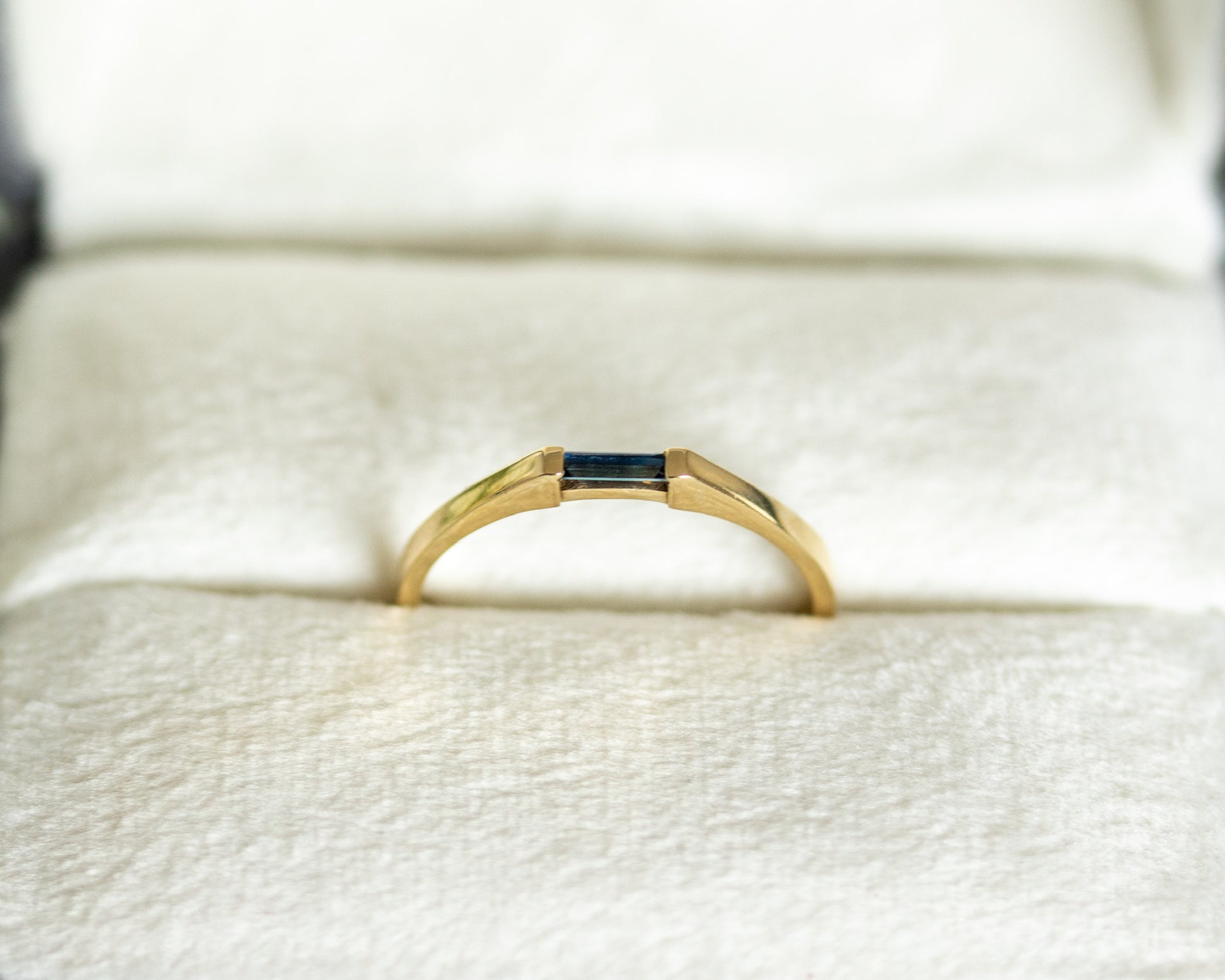 Gold ring with a central gemstone on a white cushion