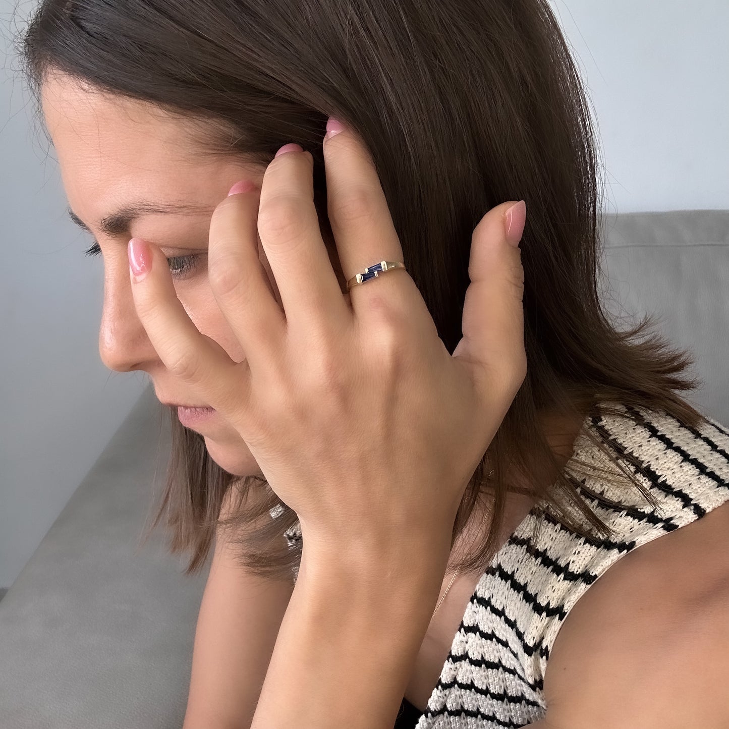 A women stroking her hair and wearing a gold ring with two blue sapphires set cheek to cheek.