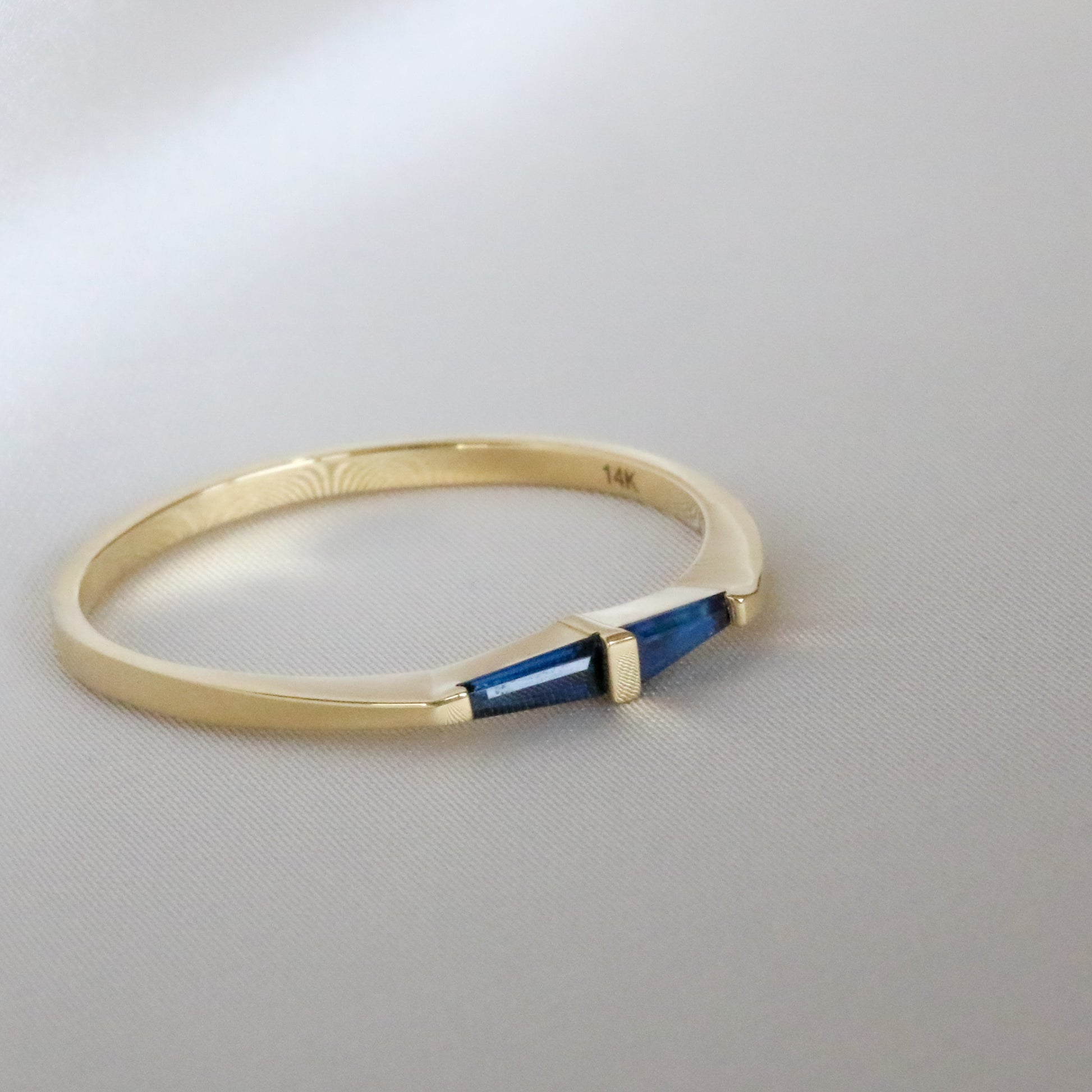 A 14K gold ring with two natural blue tapered baguette cut sapphires on white background
