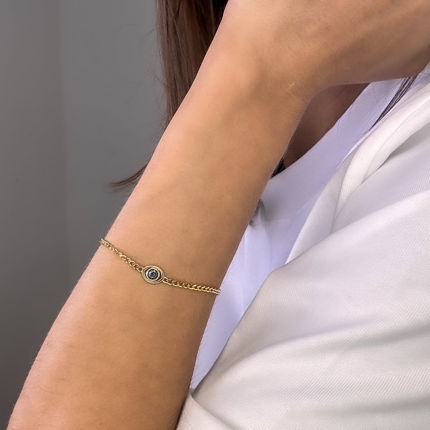 A person wearing a gold curb chain bracelet with a blue sapphire set in a evil eye centerpiece on their wrist.