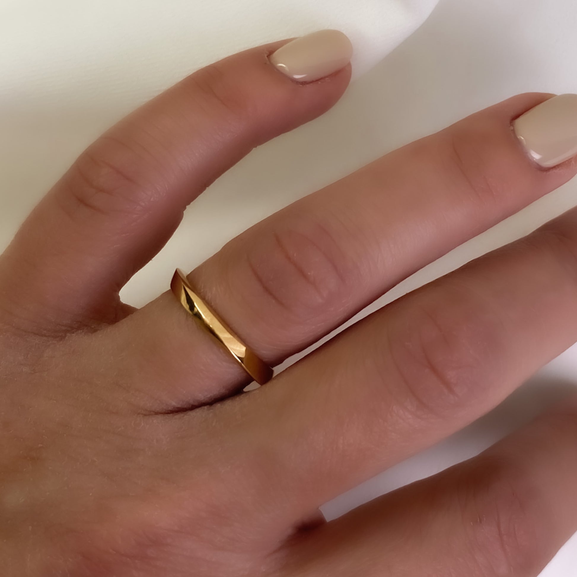 A slender, gold-colored band ring on a person's finger, showing a modern twisting design.