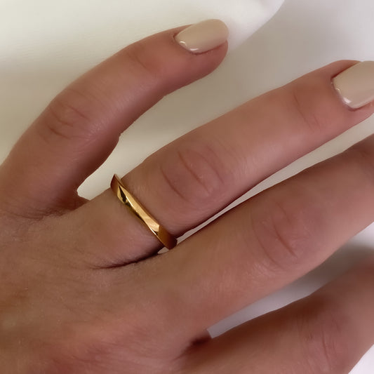 A slender, gold-colored band ring on a person's finger, showing a modern twisting design.