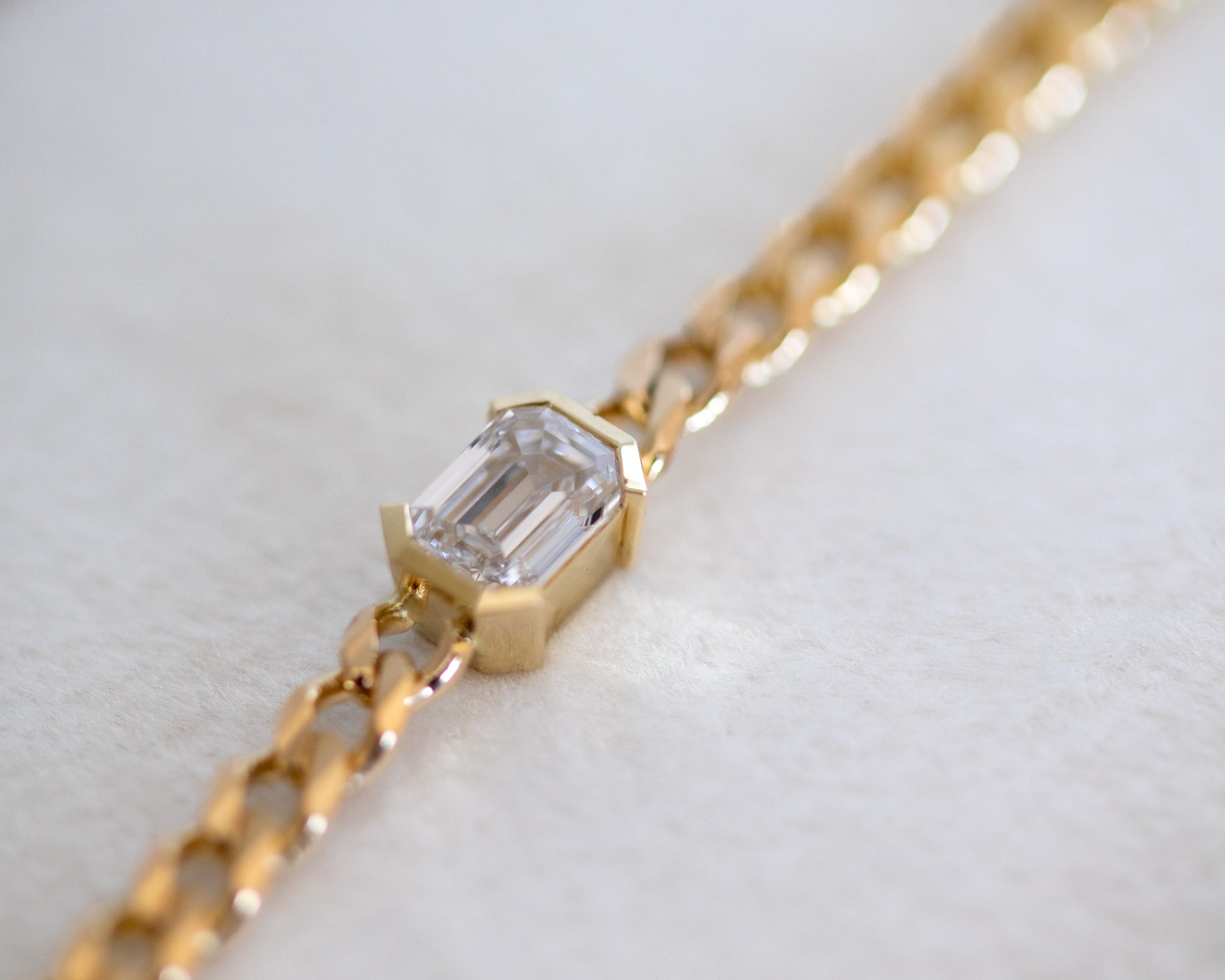 Gold curb chain bracelet with a emerald cut diamond on a light background