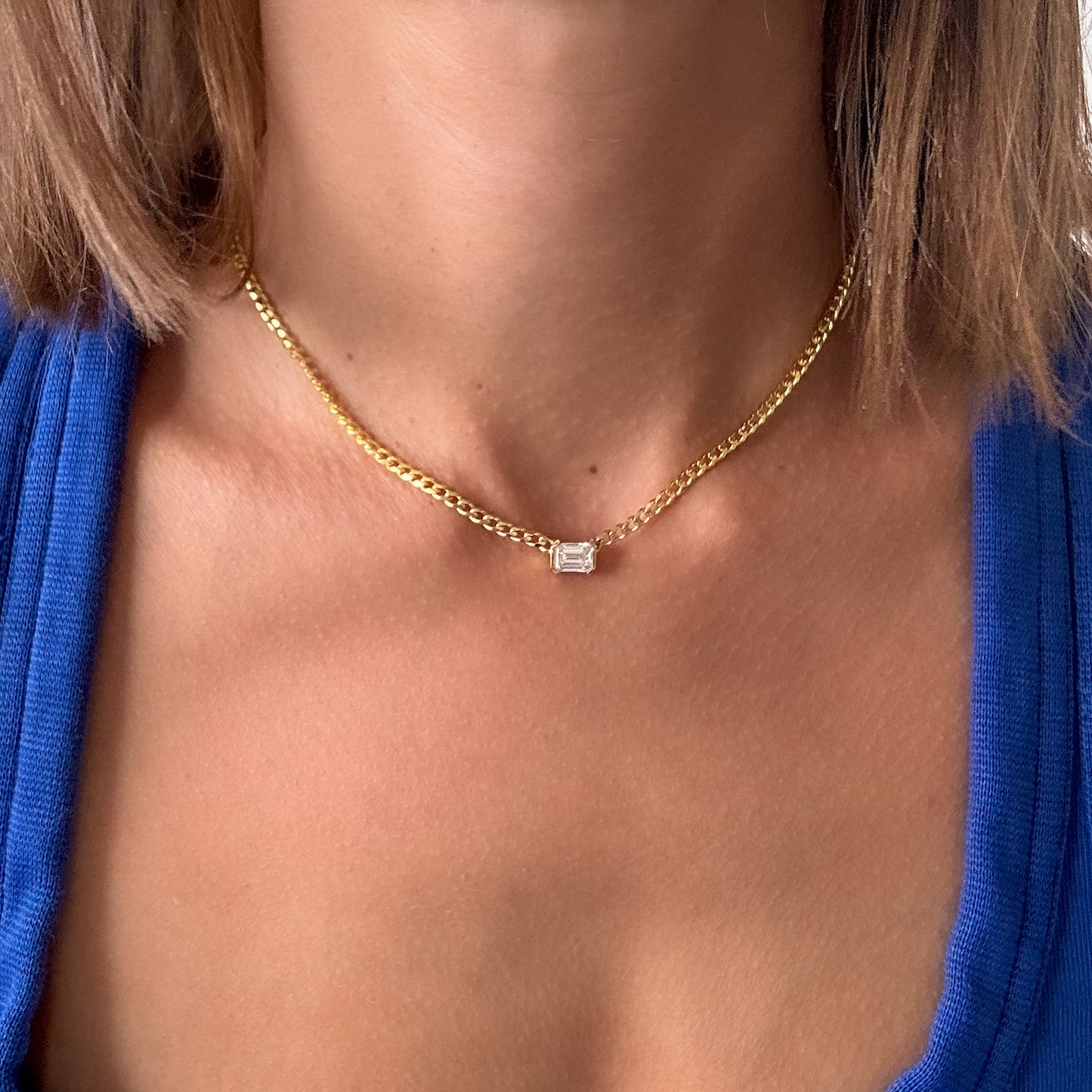 A person wearing a 14K gold diamond solitaire necklace with an emerald cut natural diamond pendant.