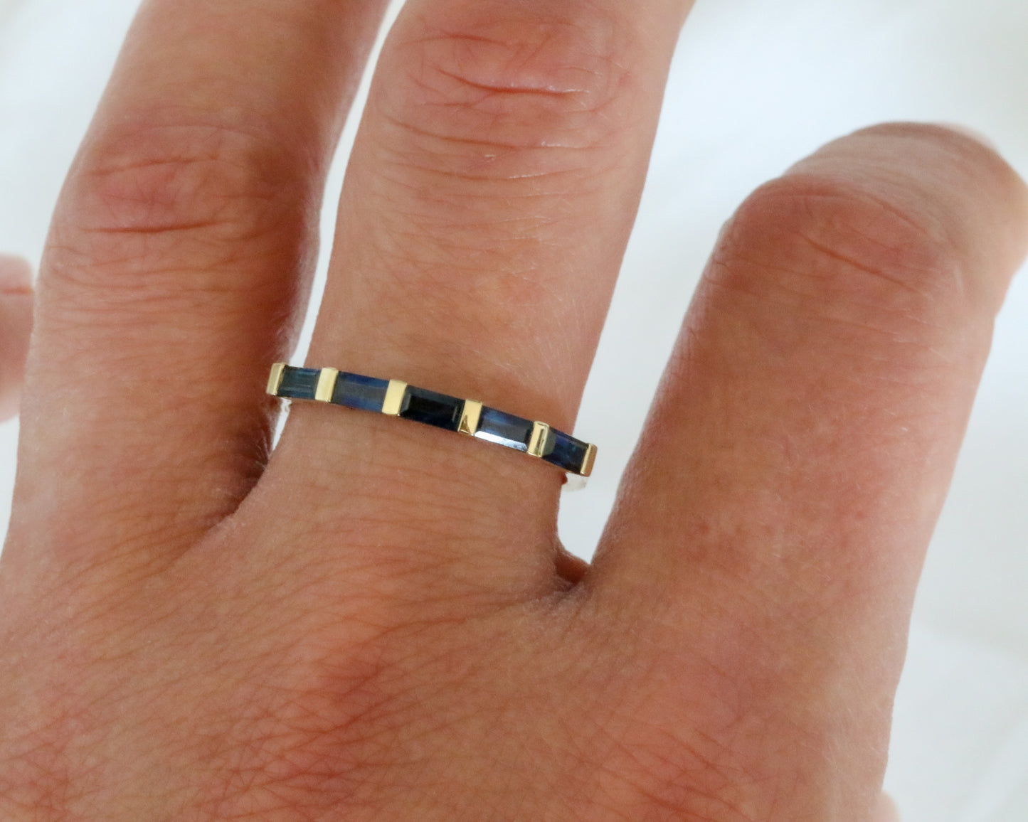 womens hand wearing 14k gold ring with baguette cut blue sapphires