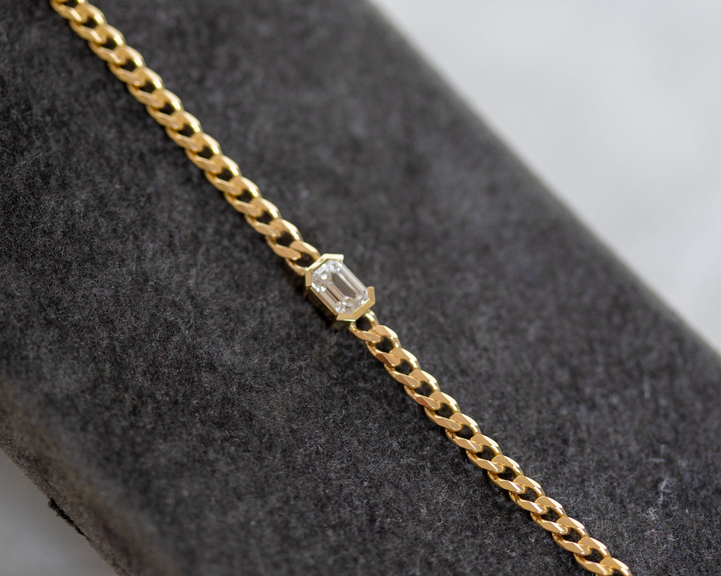 Gold bracelet with an emerald cut diamond on a gray surface
