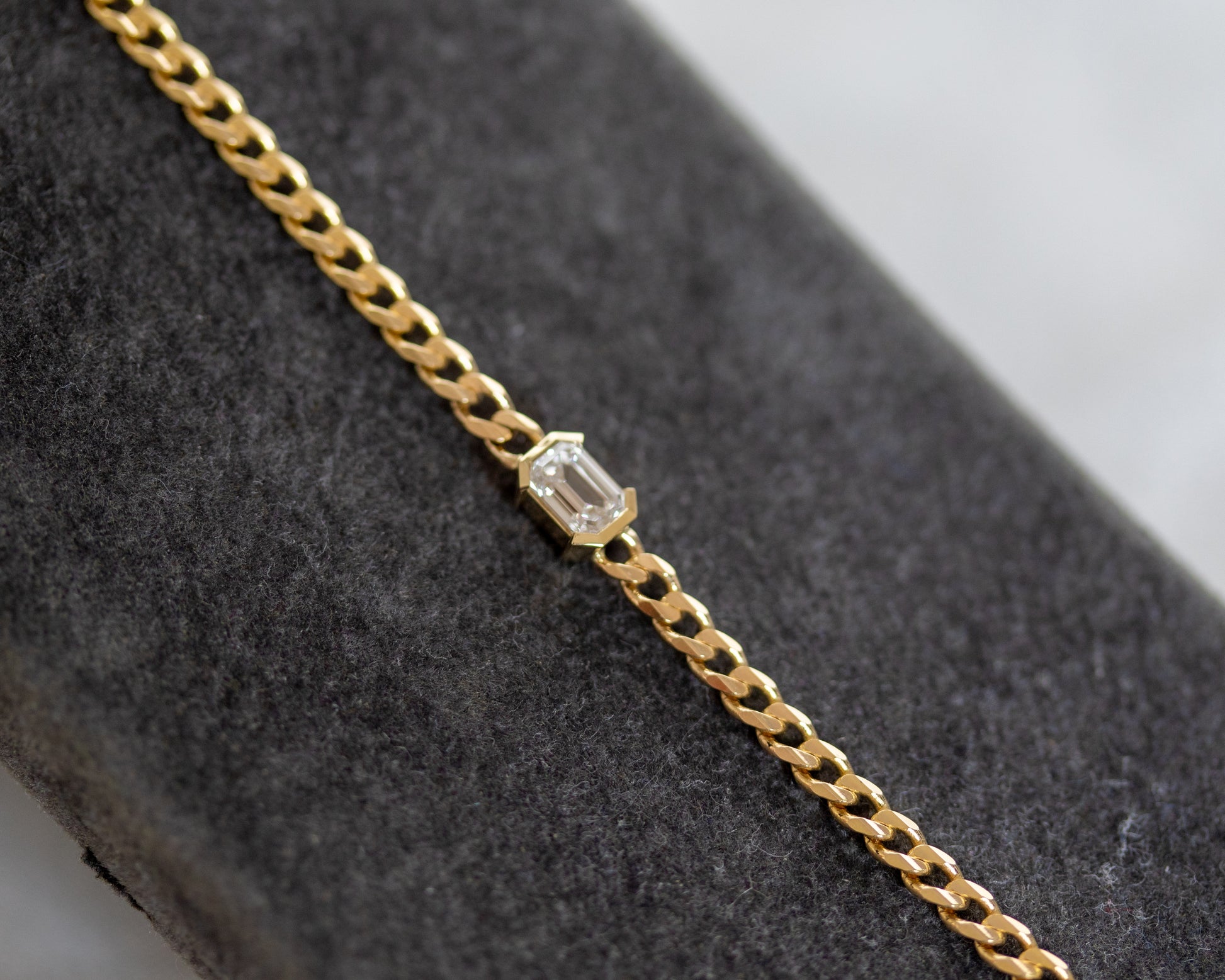 Gold bracelet with an emerald cut diamond on a gray surface