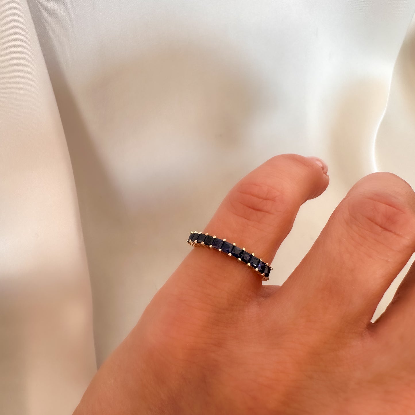 princess cut blue sapphire eternity ring displayed on women's pinky finger