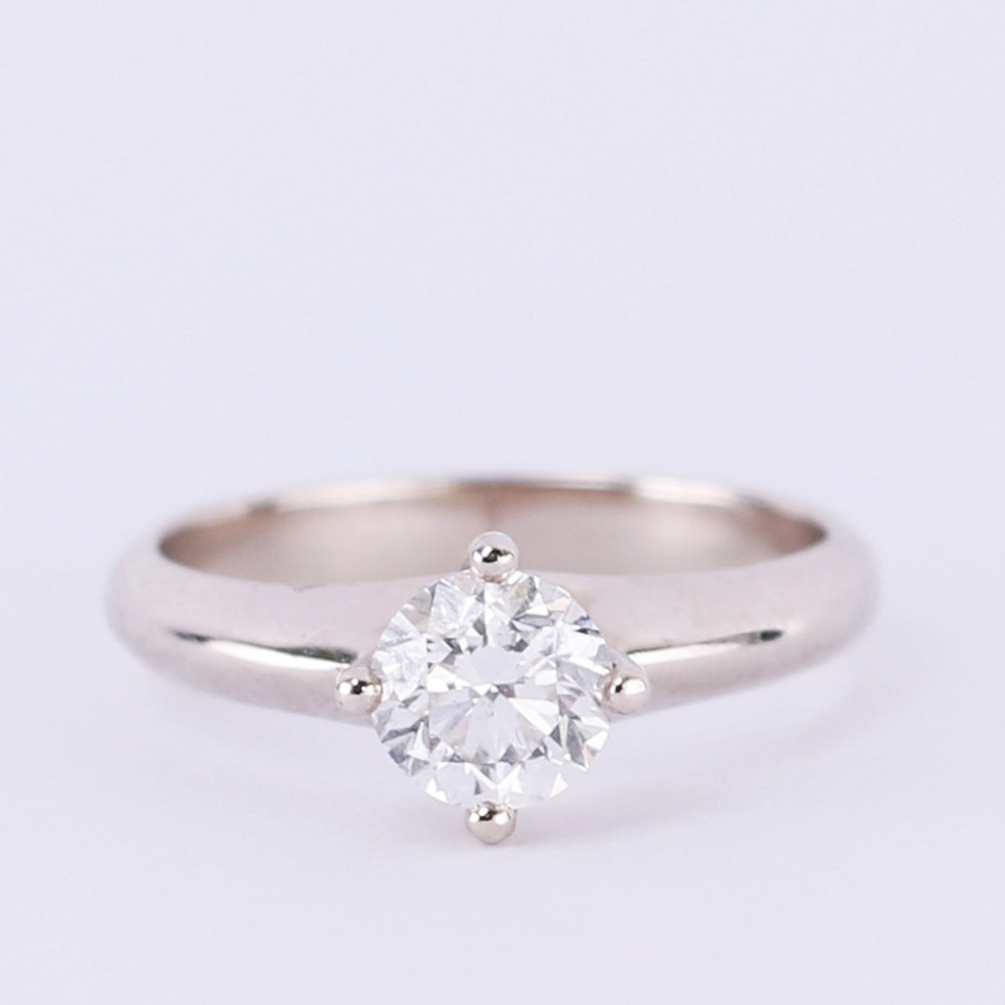 four prong solitaire diamond engagement ring on light purple background