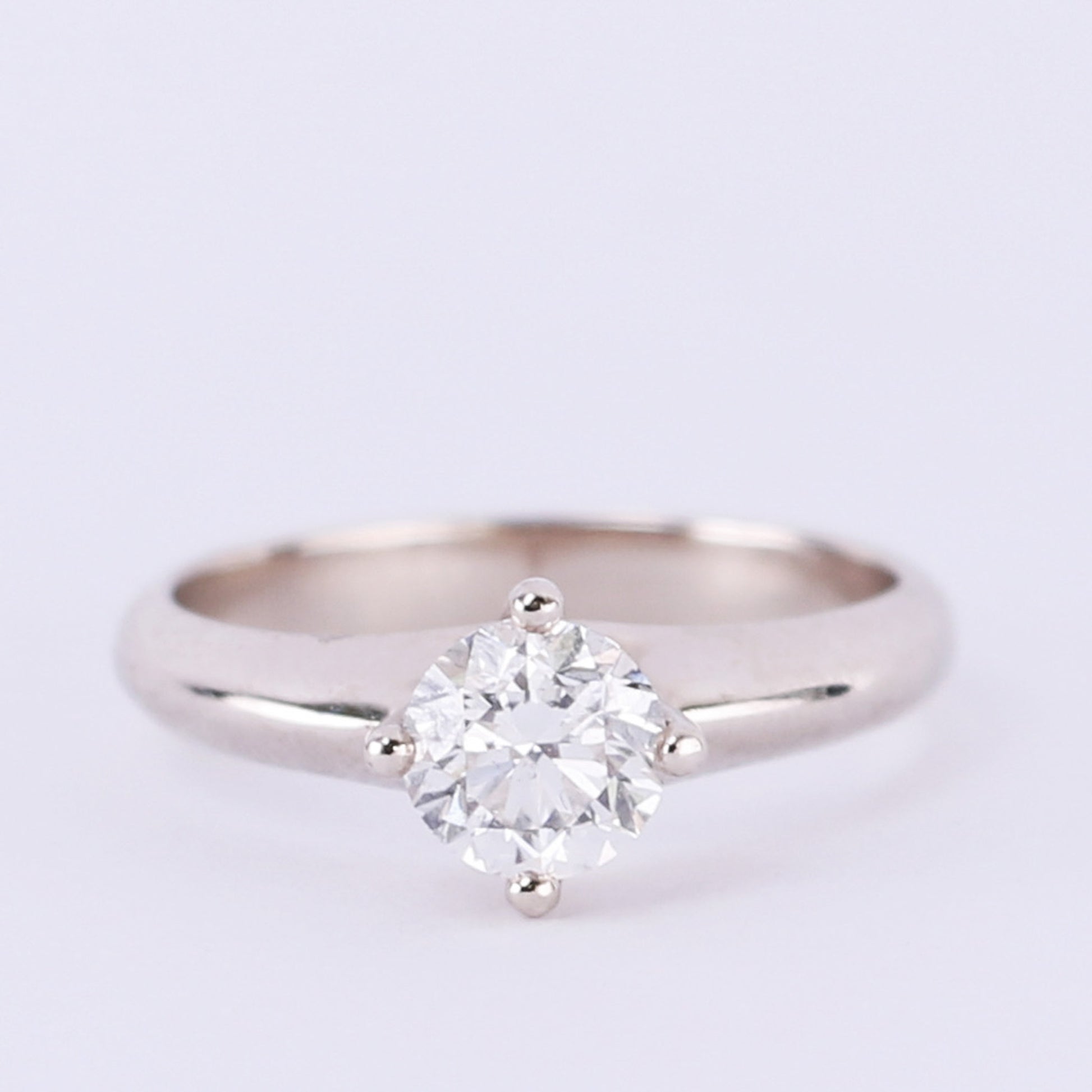 four prong solitaire diamond engagement ring on light purple background