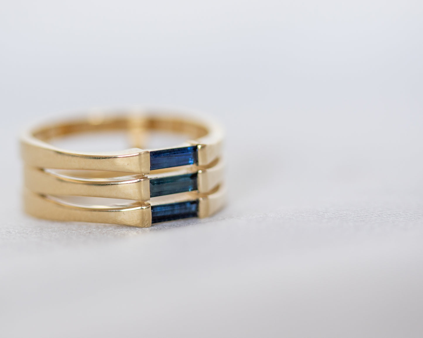 A minimalist gold ring with three blue baguette cut sapphires set close together, creating a light and unique appearance