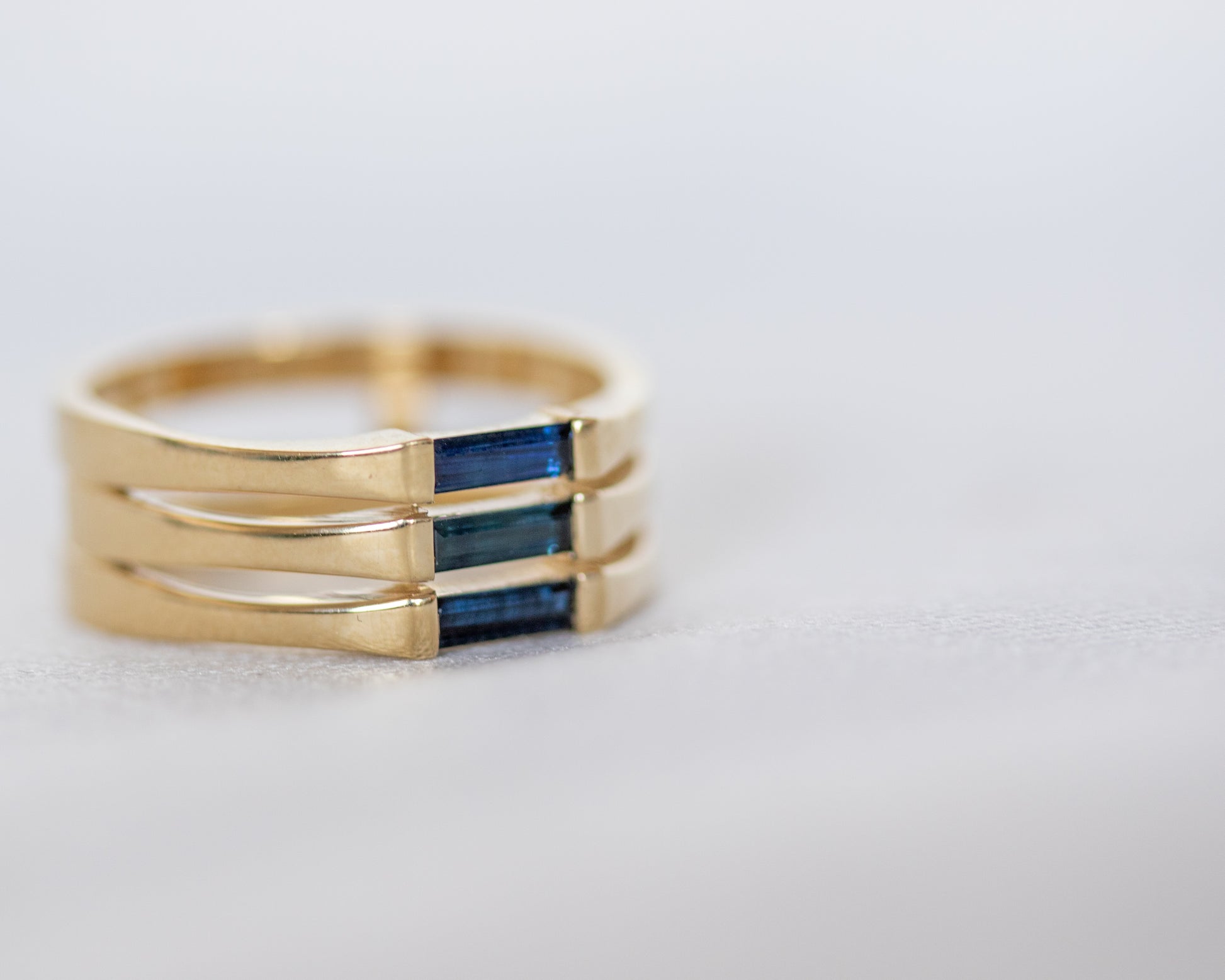 A minimalist gold ring with three blue baguette cut sapphires set close together, creating a light and unique appearance