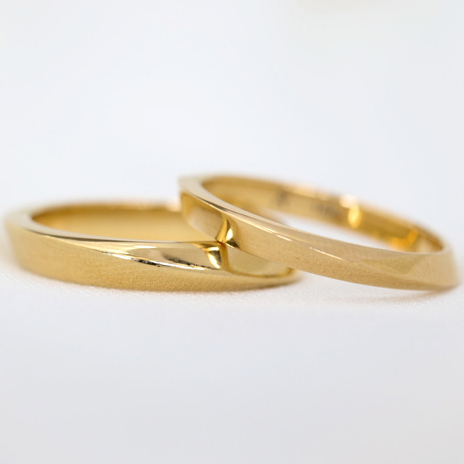 two gold geometric rings on slimmer and leaning on the other on white background