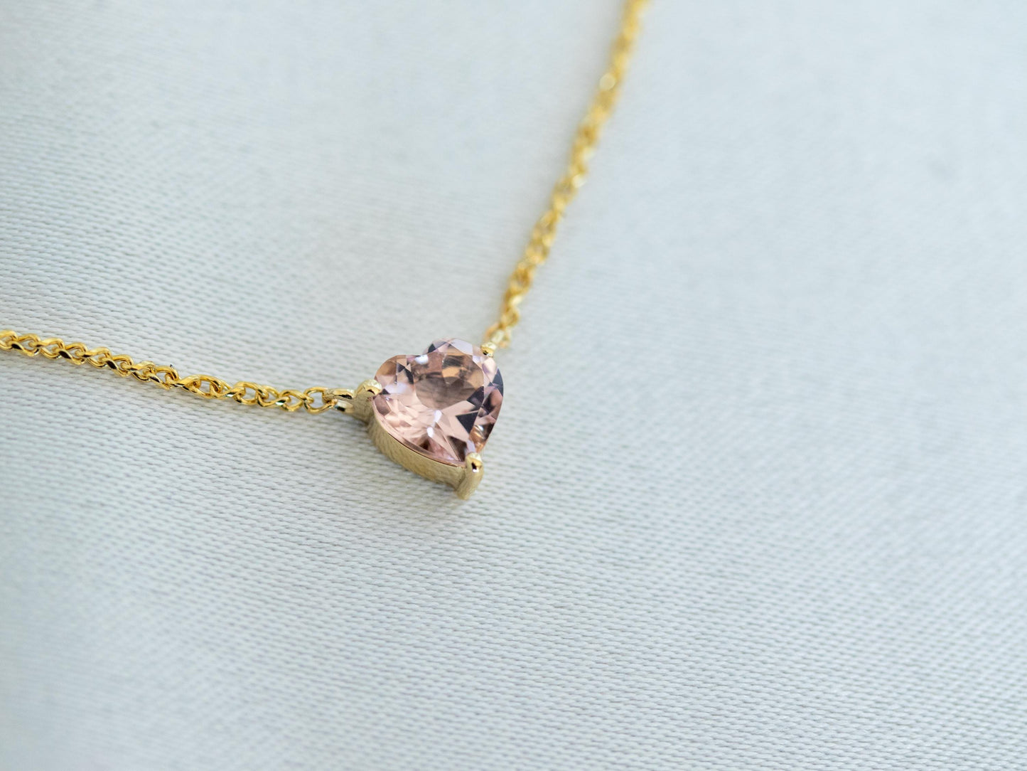 Gold necklace with a heart-shaped pink gemstone on a light blue background
