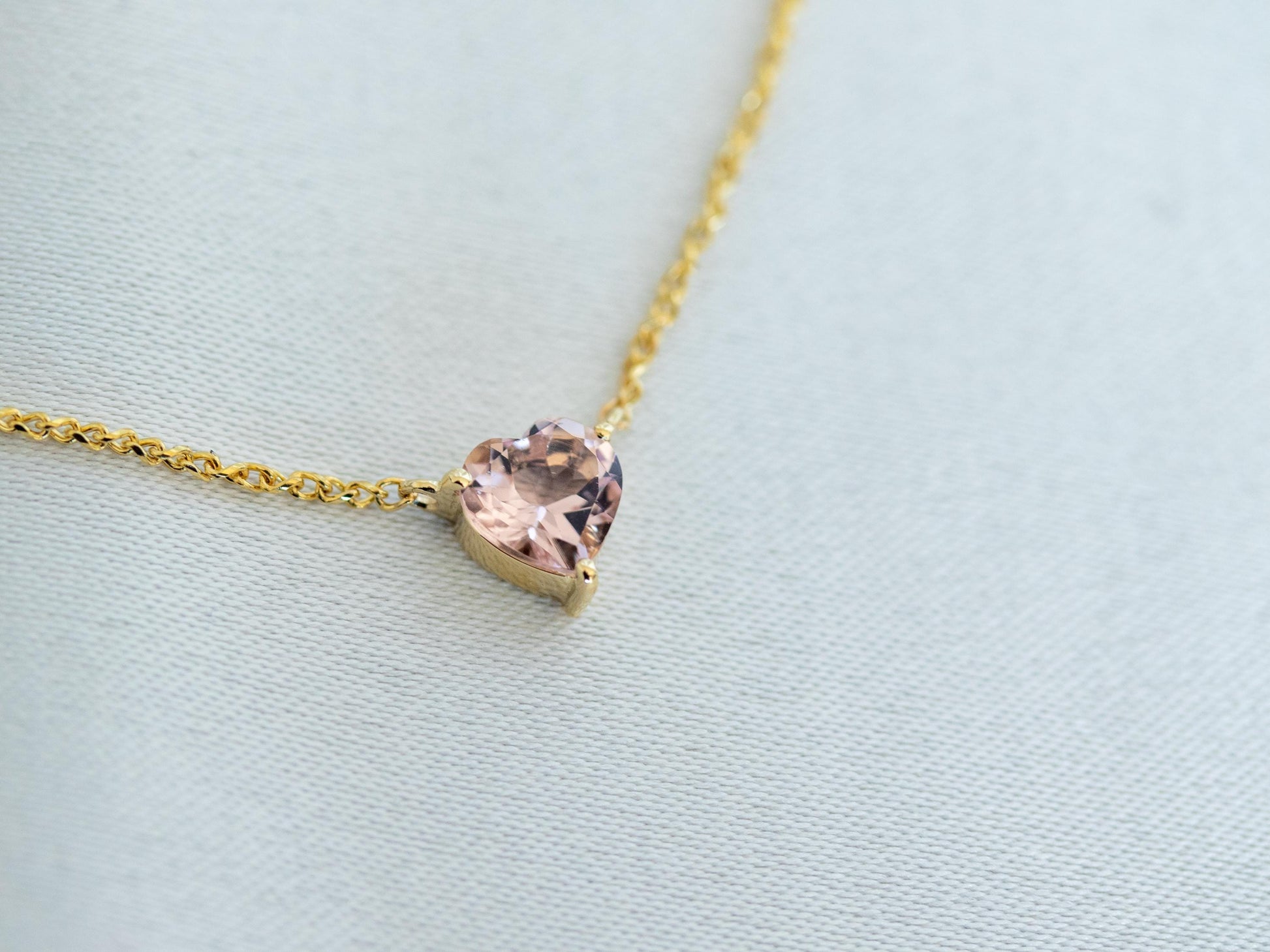 Gold necklace with a heart-shaped pink gemstone on a light blue background