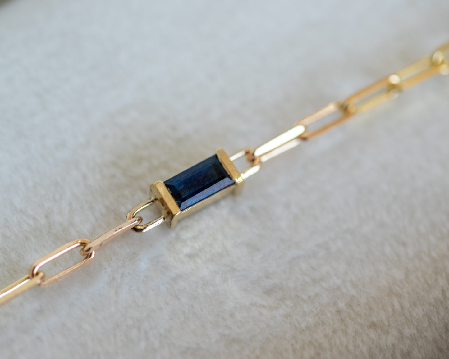 Gold bracelet with a blue baguette cut sapphire on a light gray background