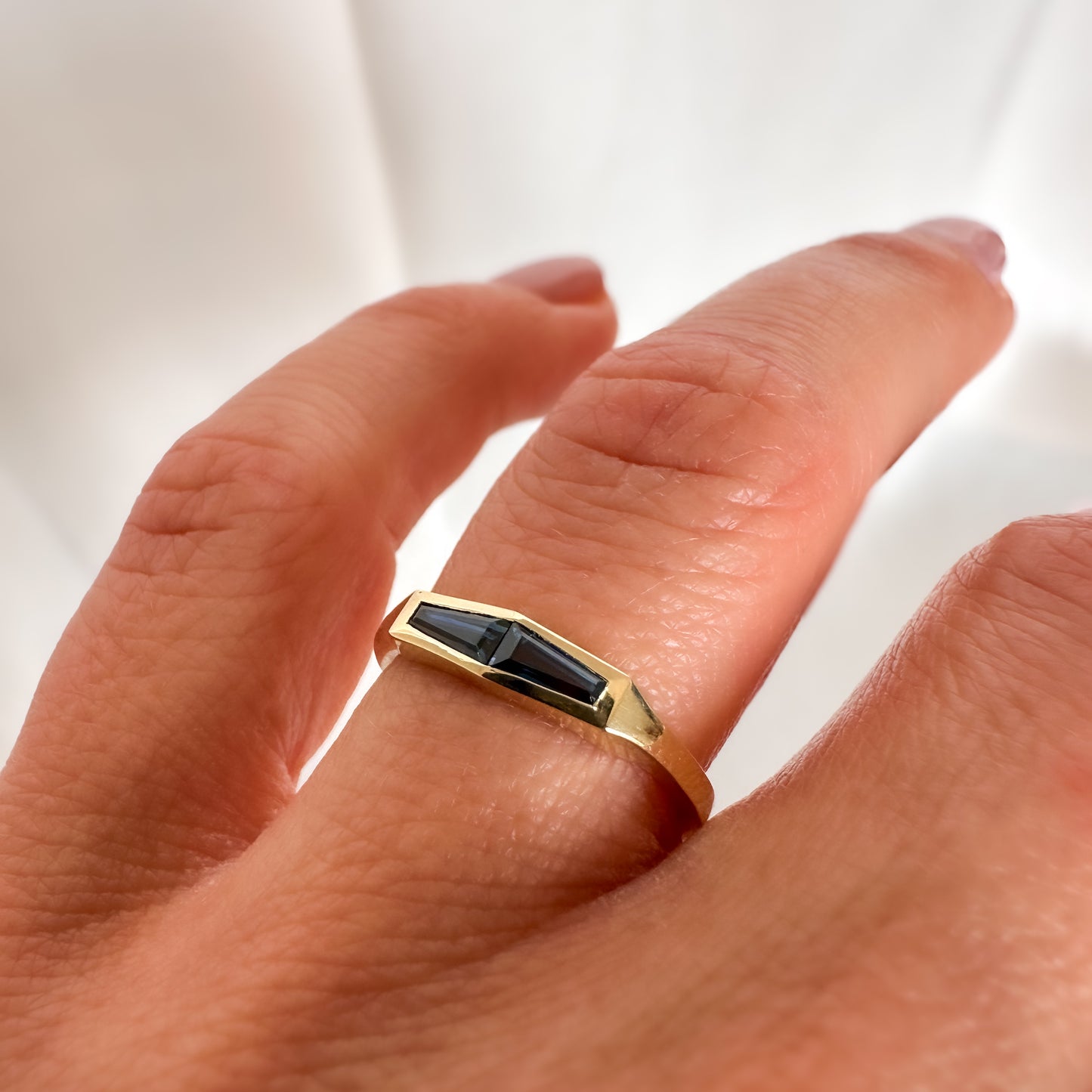 A minimalist gold ring with two blue baguette cut sapphires on womens hand