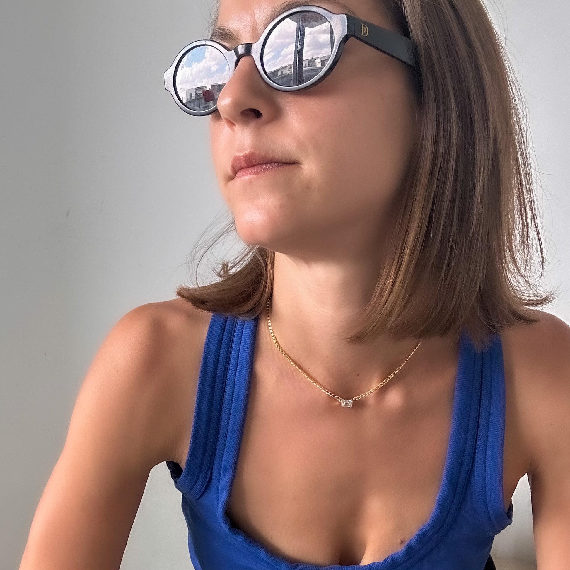 A person with sunglasses wearing a 14K gold diamond solitaire necklace with an emerald cut natural diamond pendant.