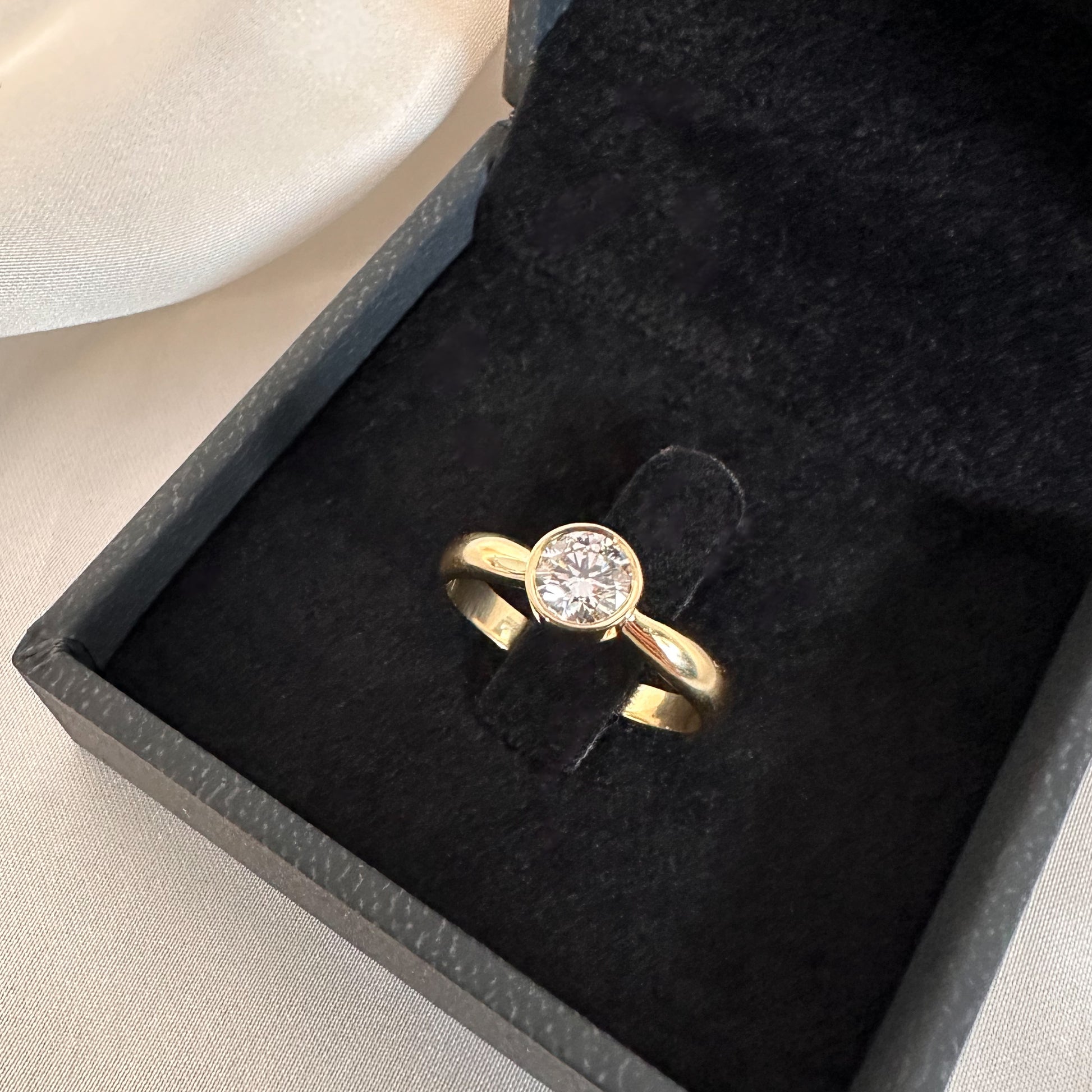 gold solitaire ring with bezel setting in black velvet box