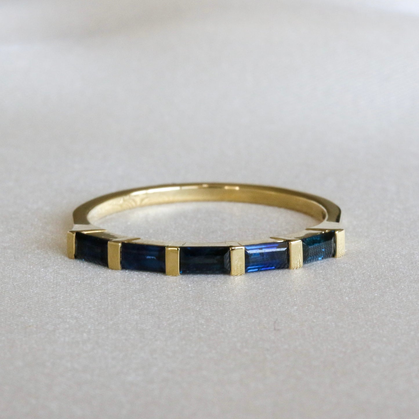 A gold stripes ring with baguette cut blue sapphires on a white surface.