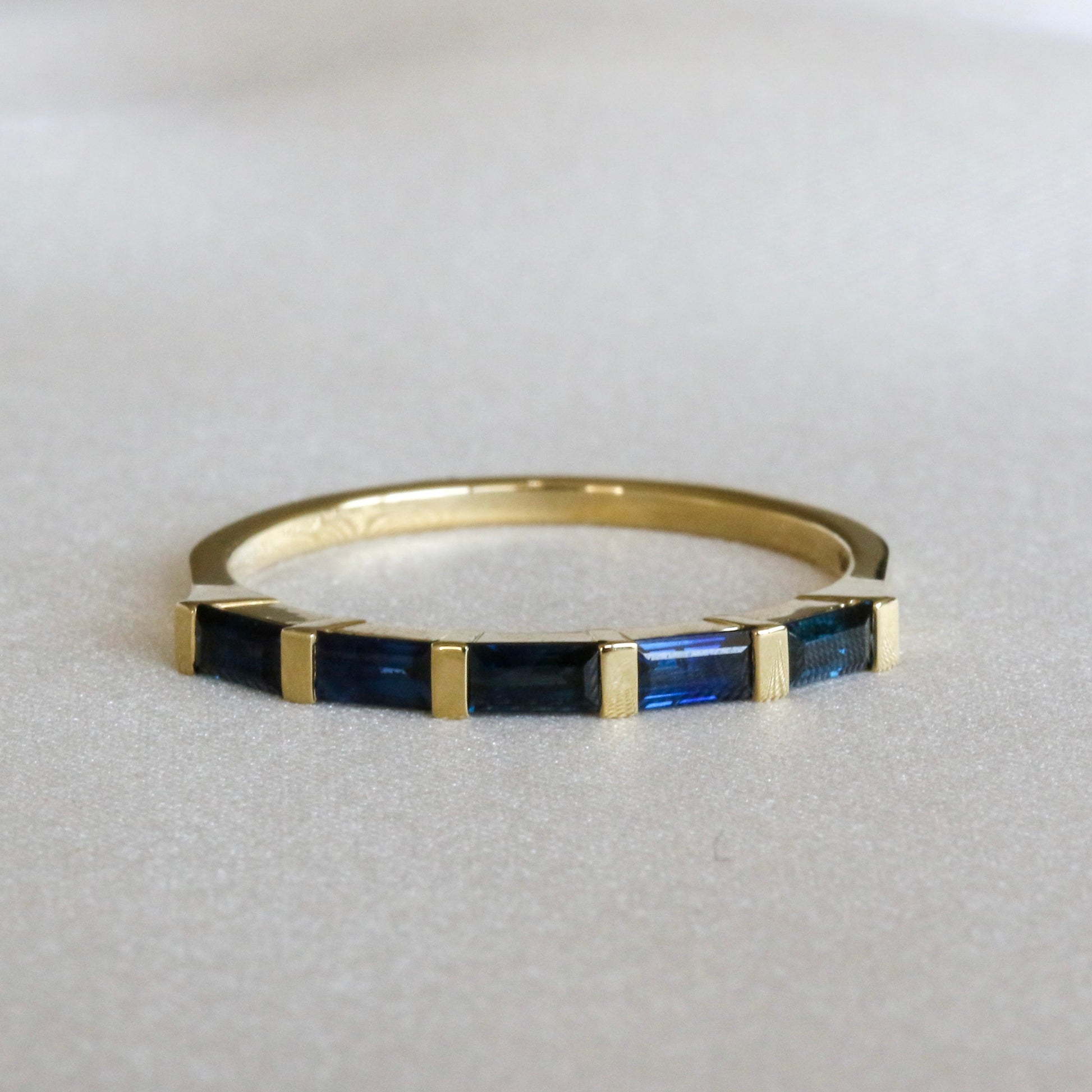 A gold stripes ring with baguette cut blue sapphires on a white surface.