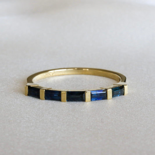 A gold stripes ring with baguette cut blue sapphires on a white surface.