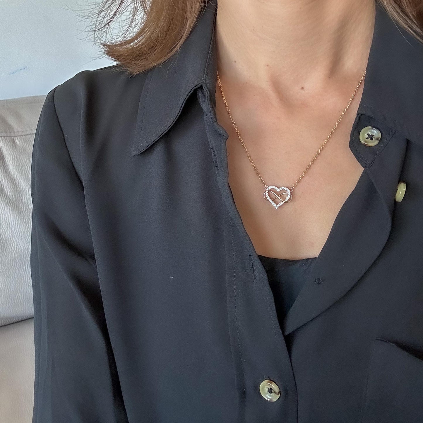 Close-up of 14K gold heart and infinity diamond pendant on neck