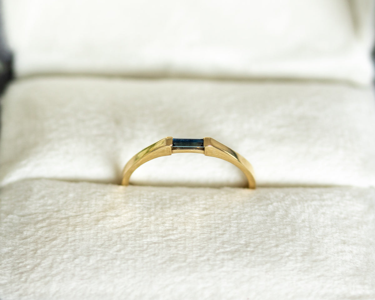 14K yellow gold needle baguette blue sapphire ring in a cream jewelry box, front view
