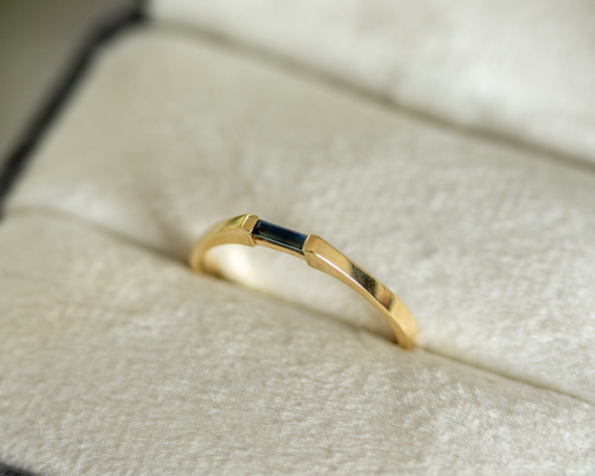 14K yellow gold needle baguette blue sapphire ring in a cream jewelry box