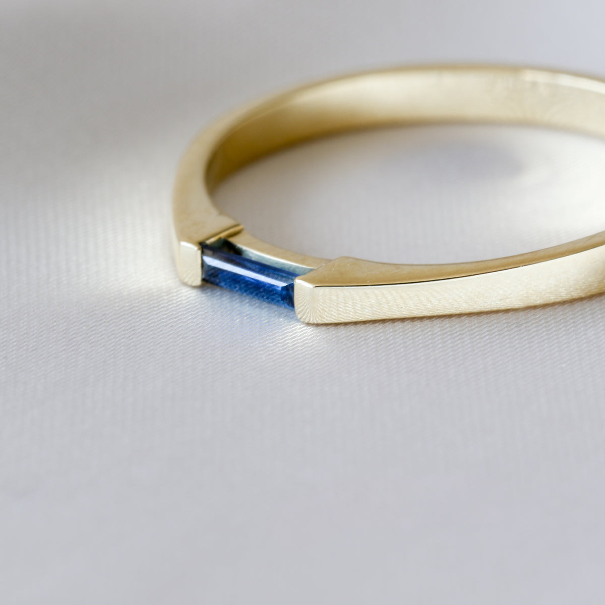 Side view of a 14K yellow gold ring with a needle baguette blue sapphire, on white