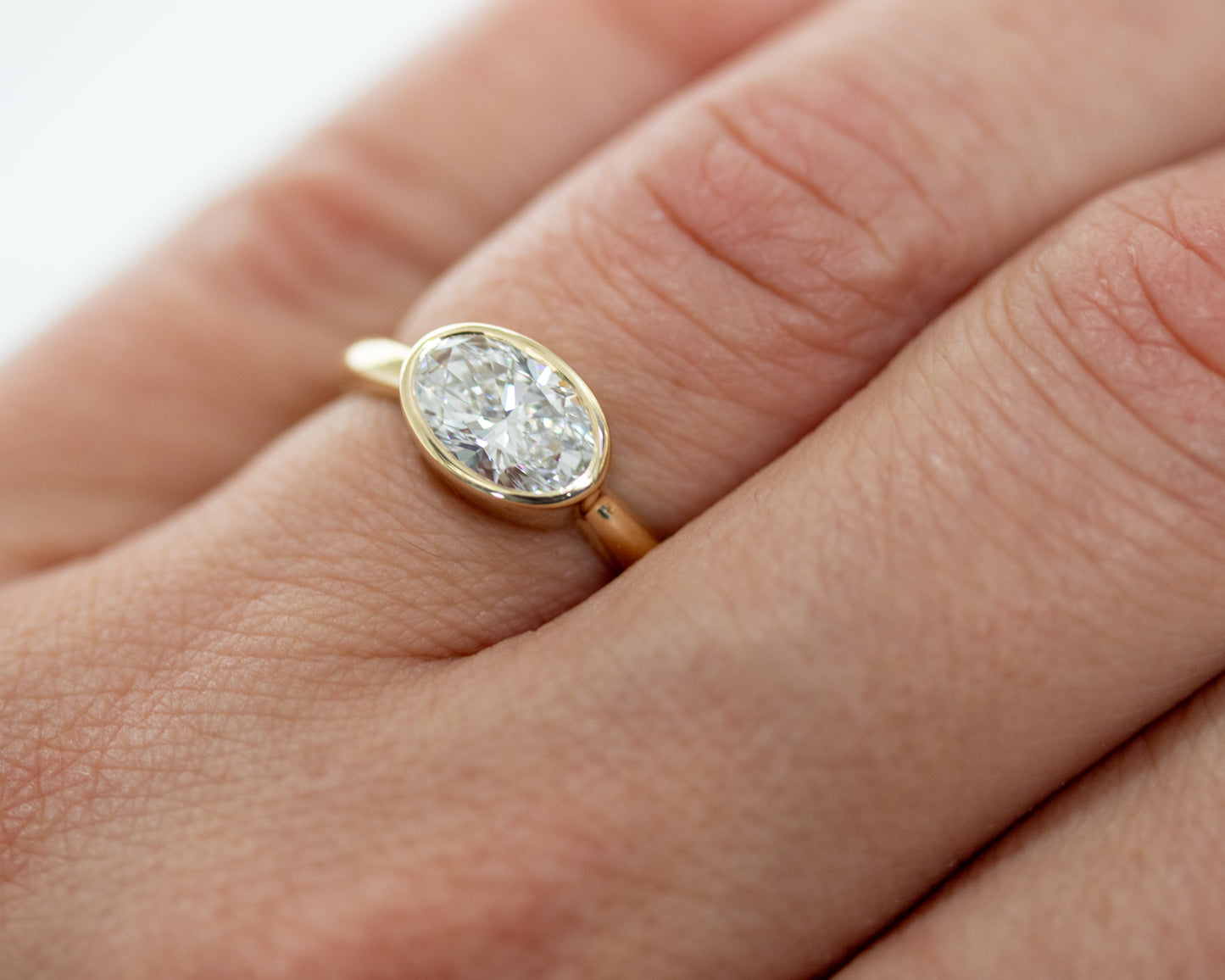 Oval diamond engagement ring on hand — solid 14K yellow gold bezel-set solitaire, elegant everyday fine jewelry.