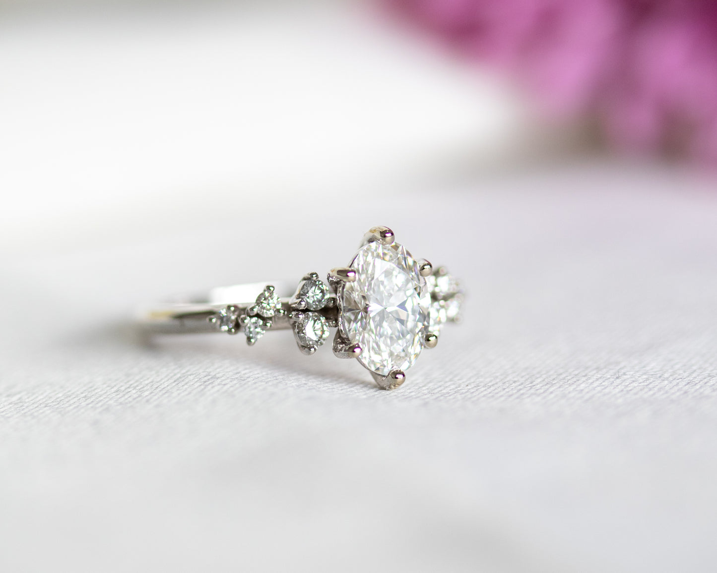Close-up of an oval diamond engagement ring with a cluster of diamonds on either side, in white gold.