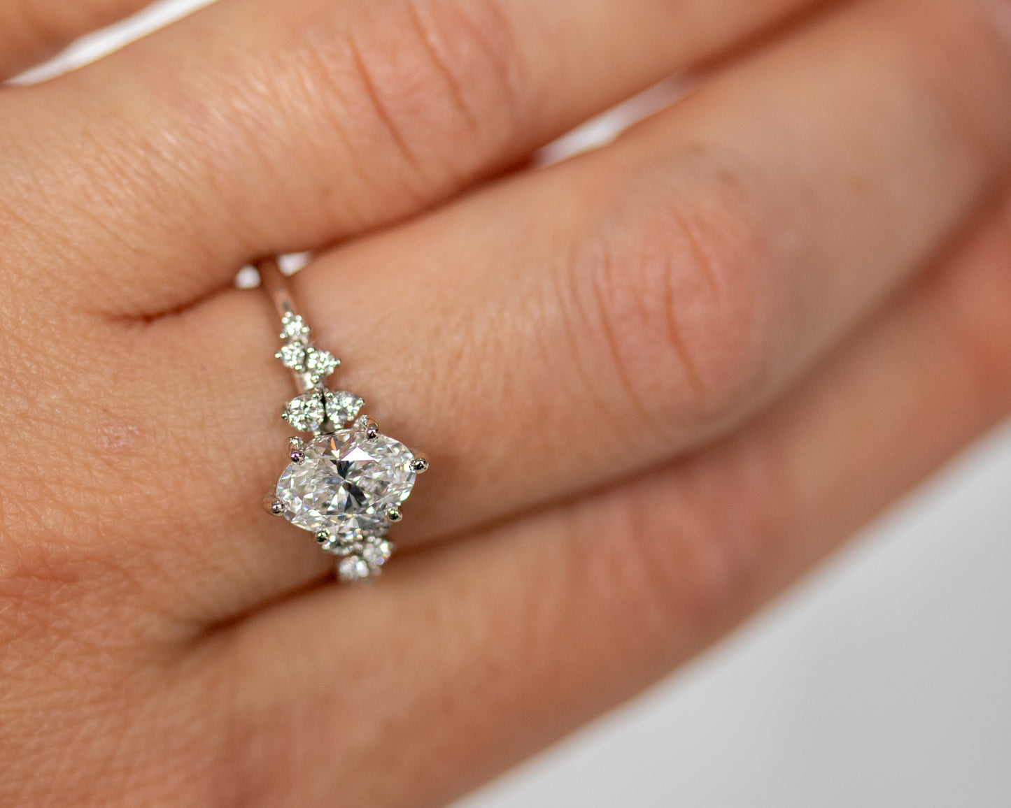 Close-up of an oval diamond engagement ring worn on a finger.