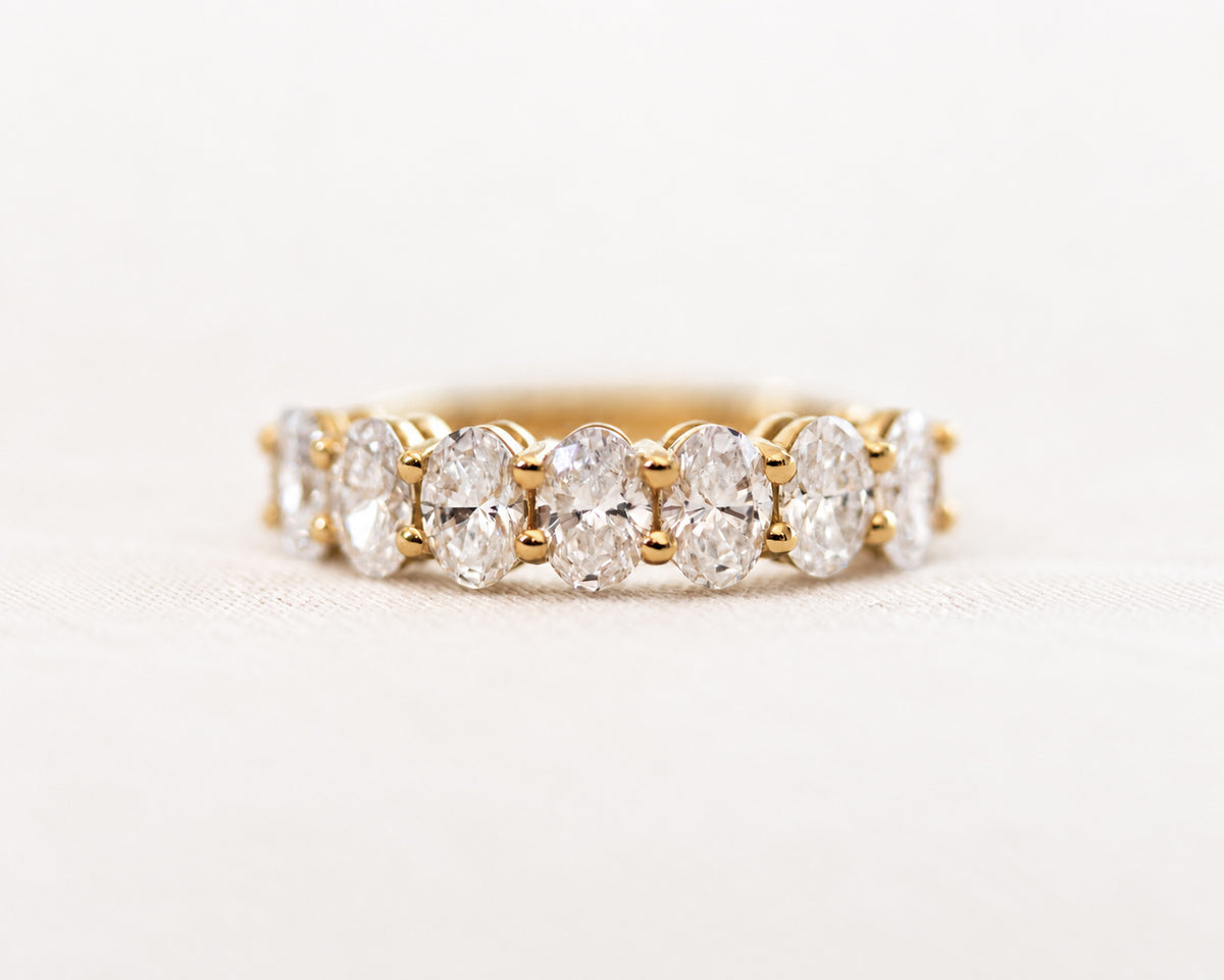 Seven-stone oval-cut diamond ring in gold, angled view on a light surface